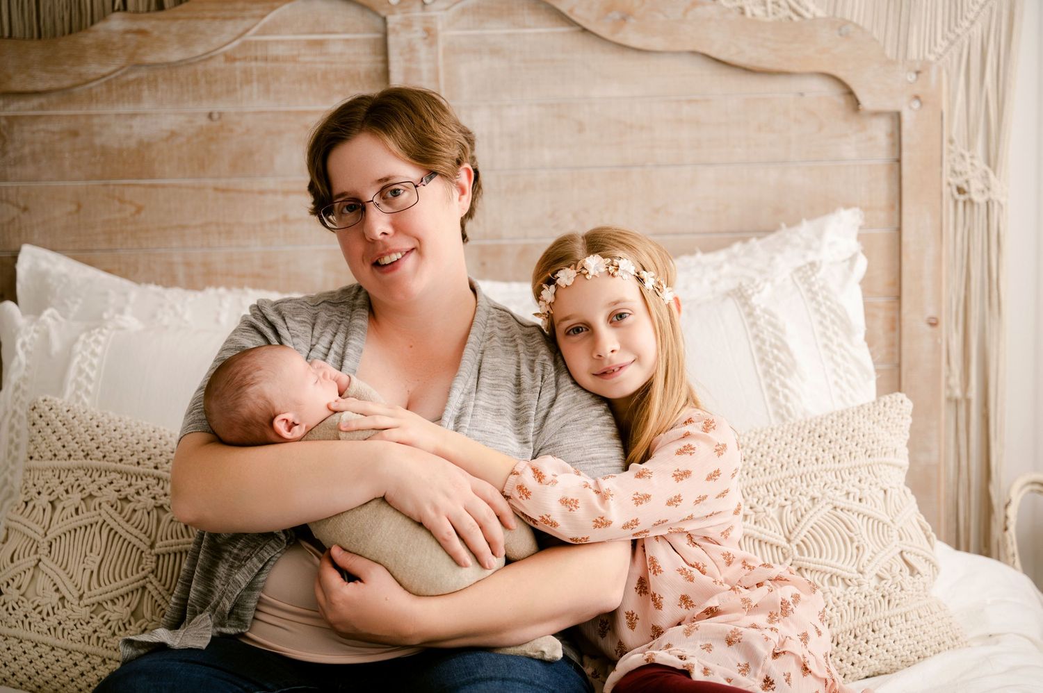 A cozy family moment captured on a bed with cream pillows and a vintage headboard in soft lighting.