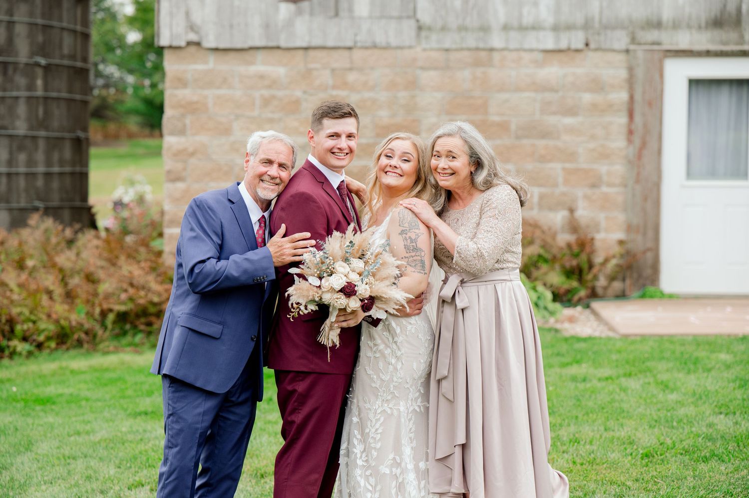 Wedding group photo with family members in coordinated formal attire outside brick building.