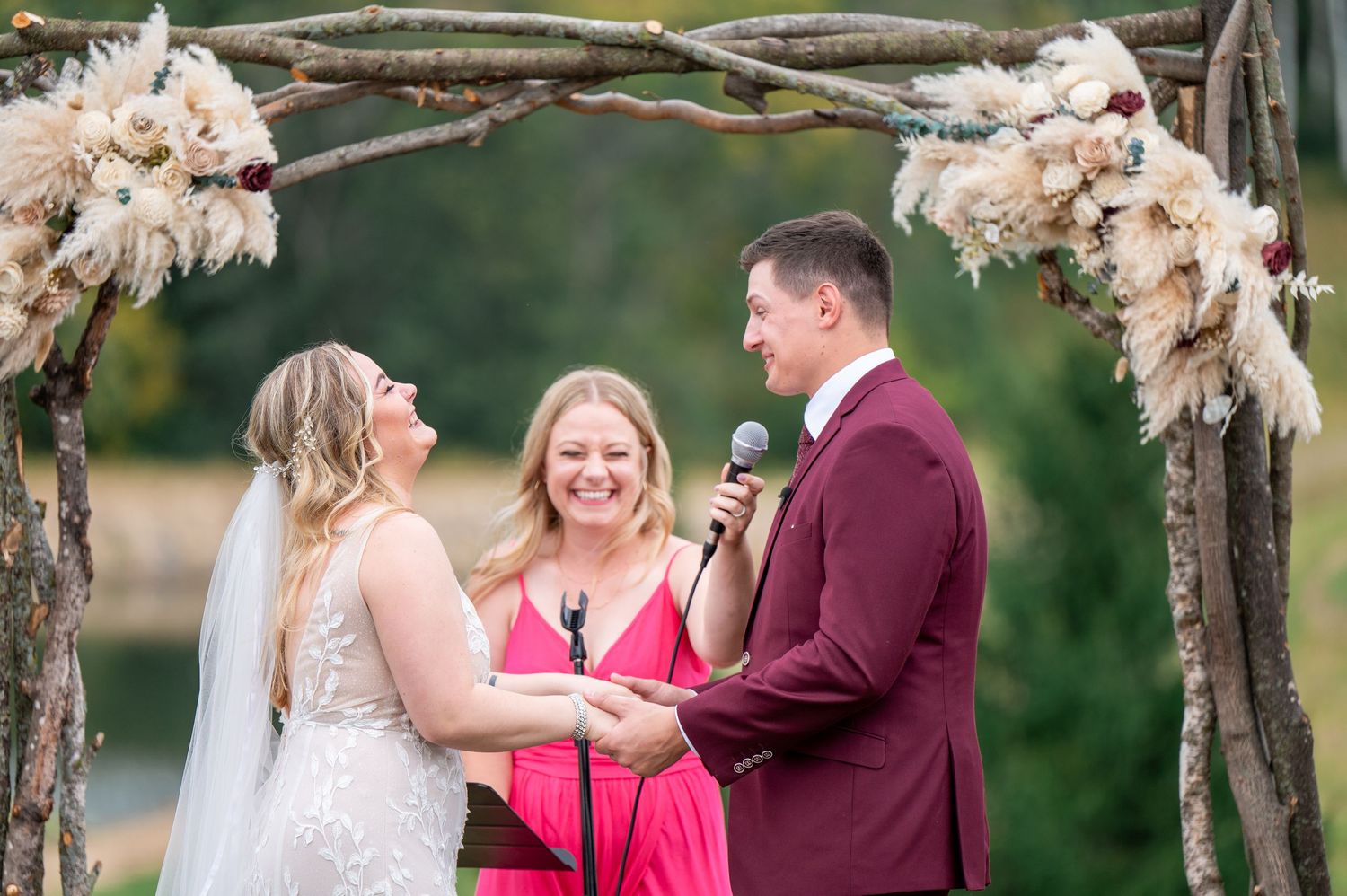 A couple stands with their officiant under a rustic arch during their outdoor wedding ceremony.