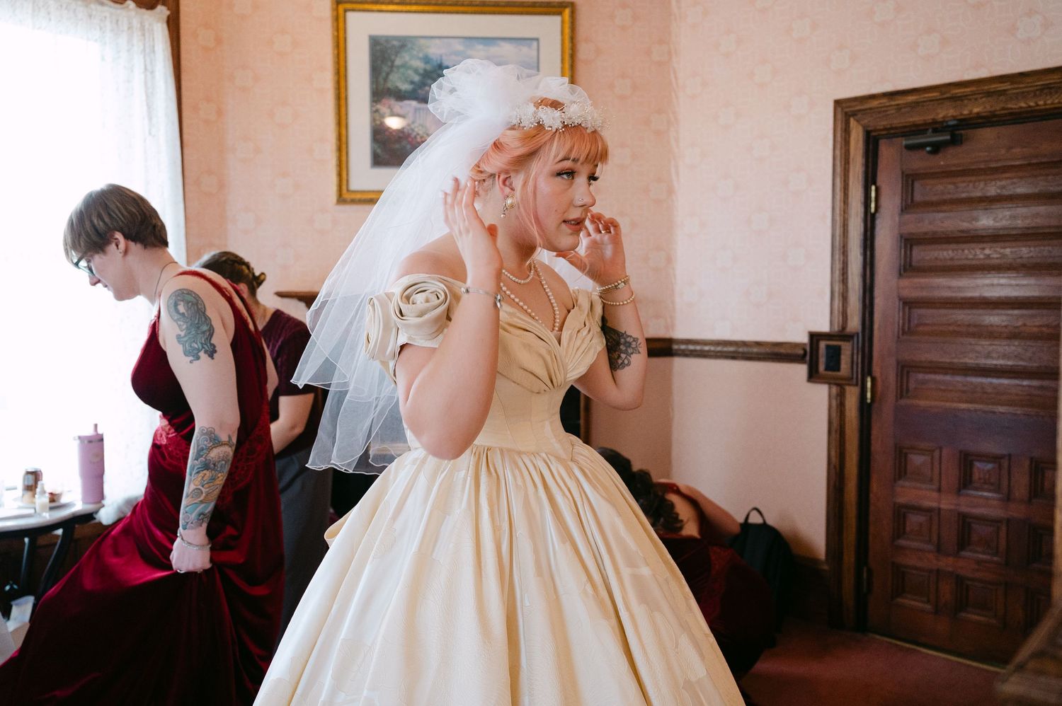 Central MN Wedding Photos | Bride in a vintage cream ballgown adjusting her veil while bridesmaid gets ready in background.