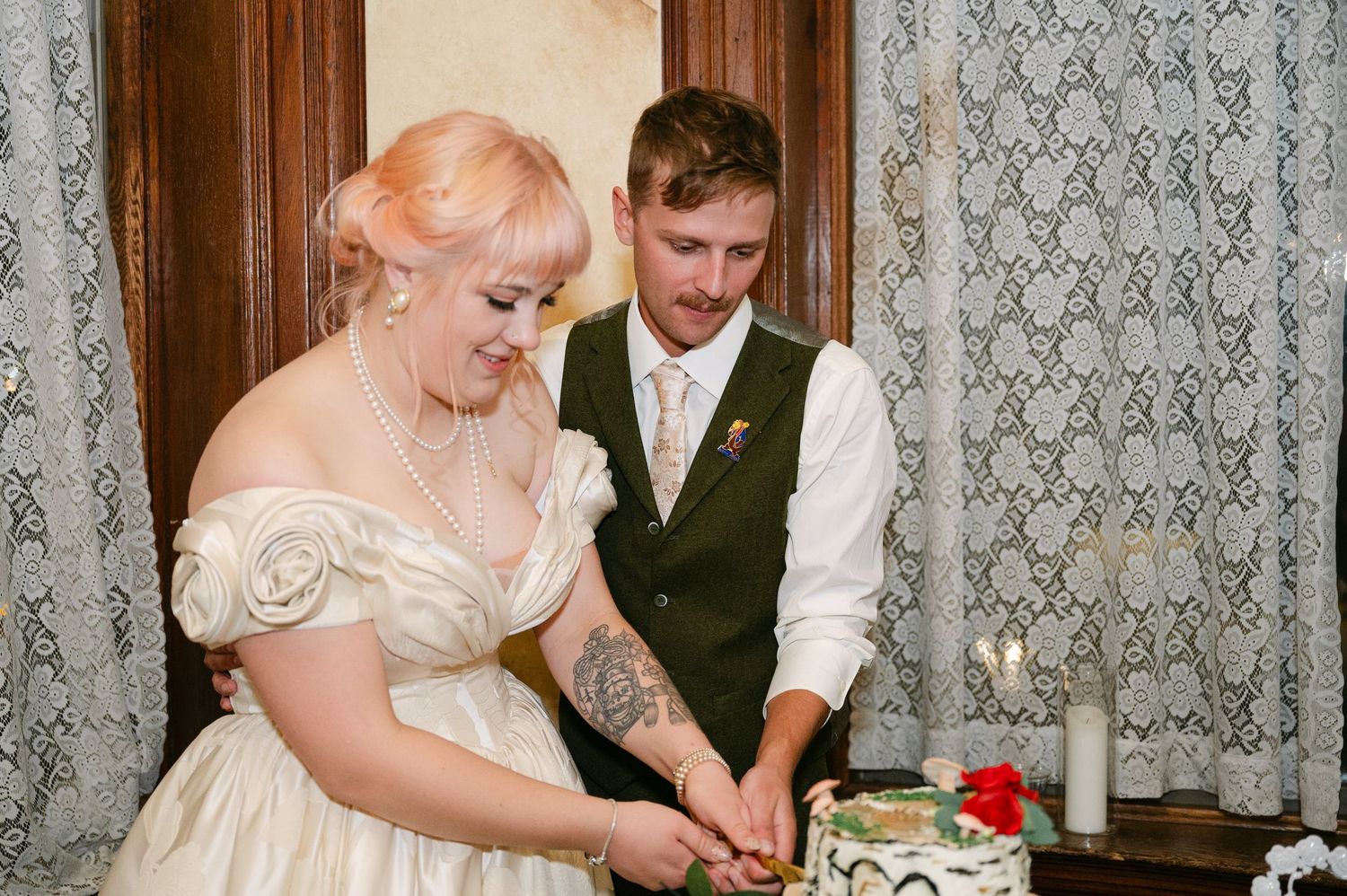Central MN Wedding Photos | Bride and groom cutting wedding cake together at reception in vintage decorated venue.