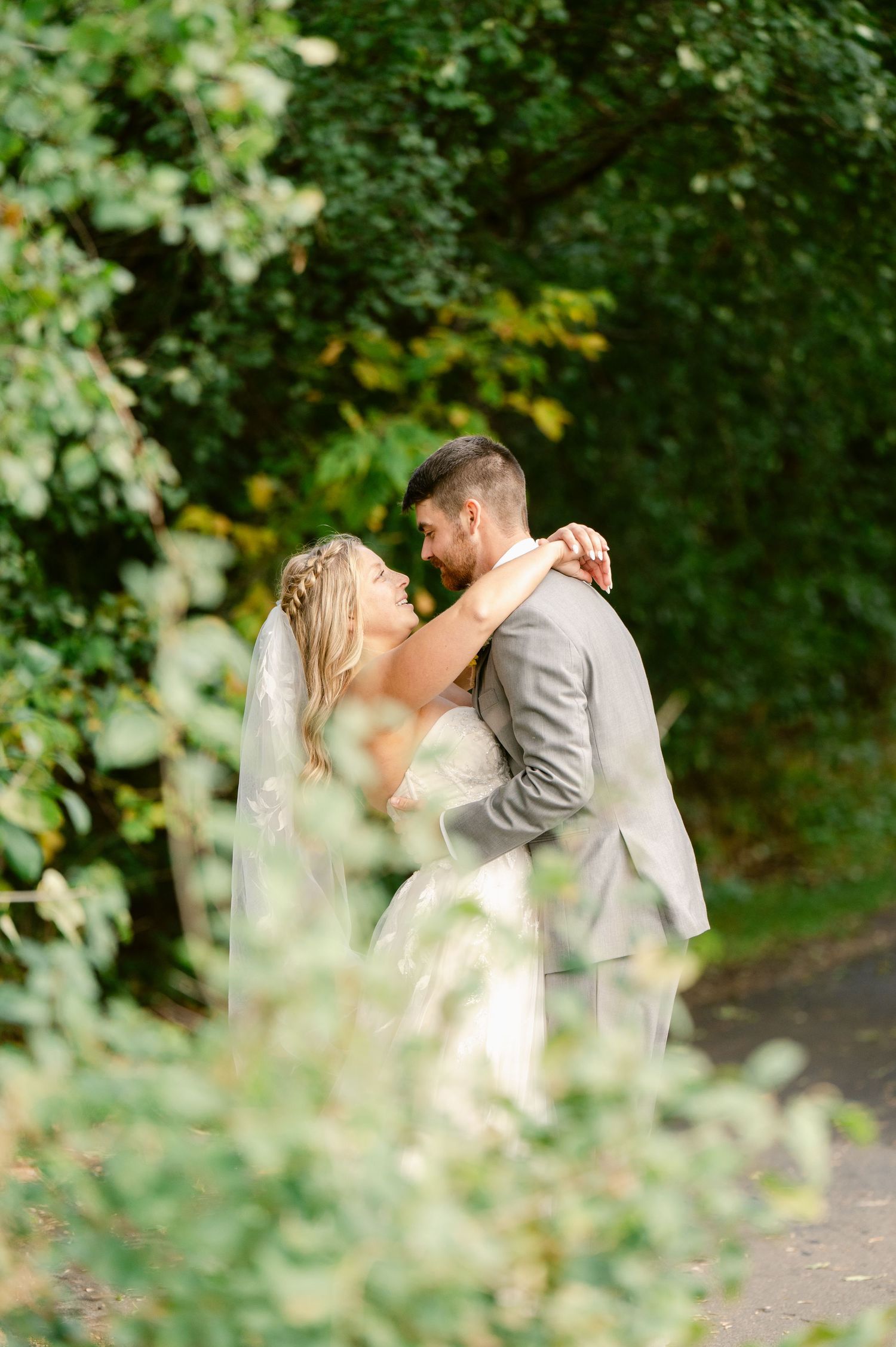 Central MN Wedding Photos | Bride and groom embracing in lush green garden during wedding portraits.