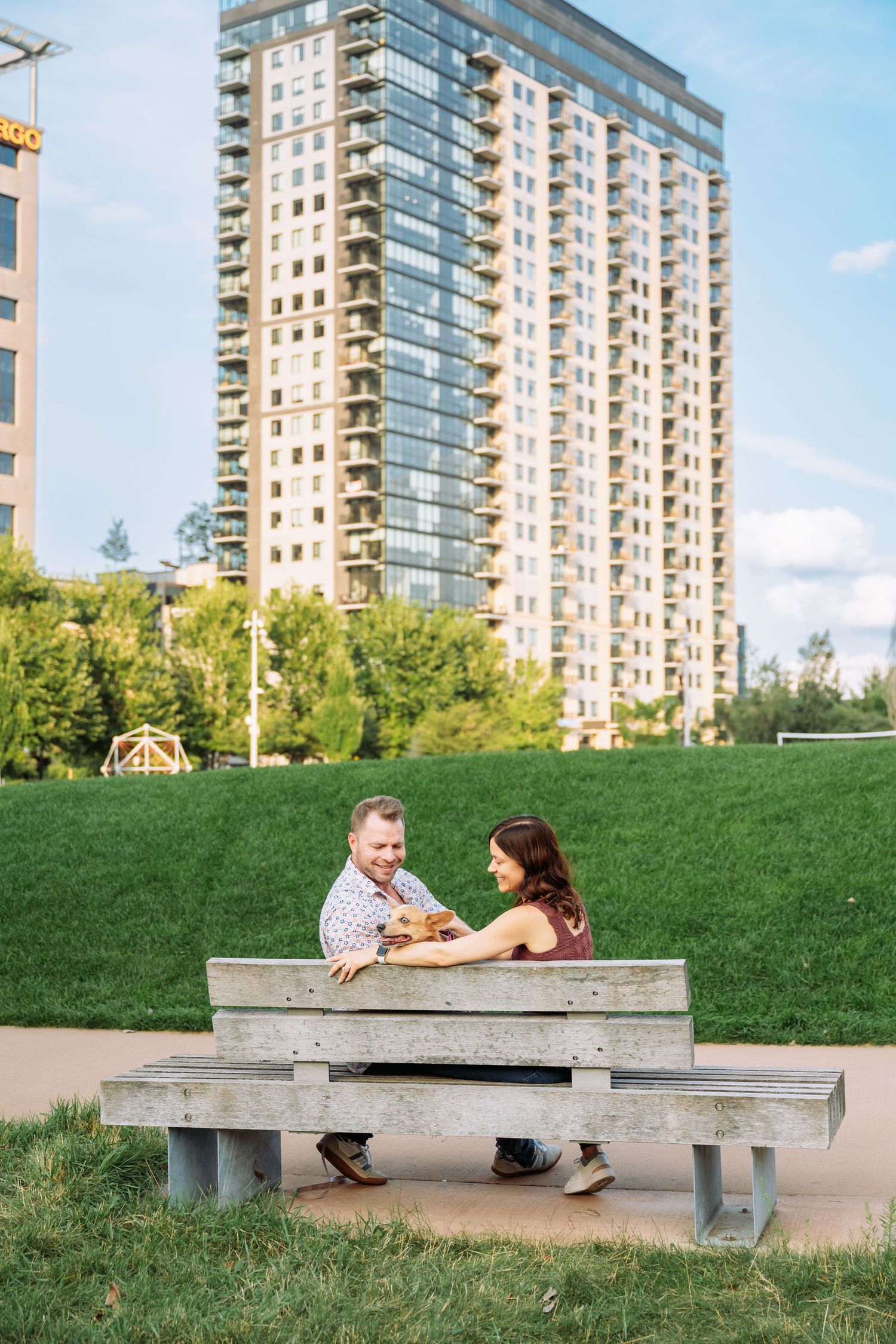 A couple relaxes on a concrete bench with modern high-rise apartment buildings in the background.