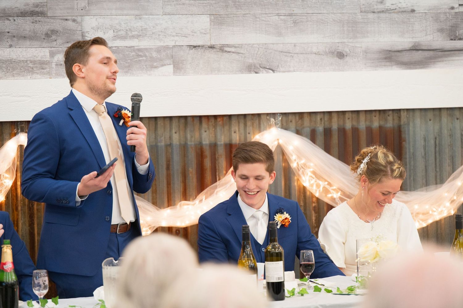 Wedding guests react with laughter and joy during an emotional reception speech at an outdoor venue.