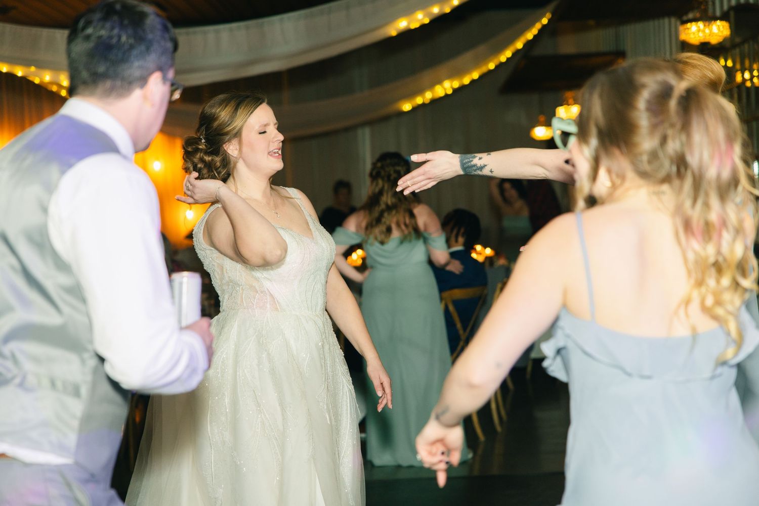 Bride in sage green gown dances joyfully with wedding guests during festive reception celebration.