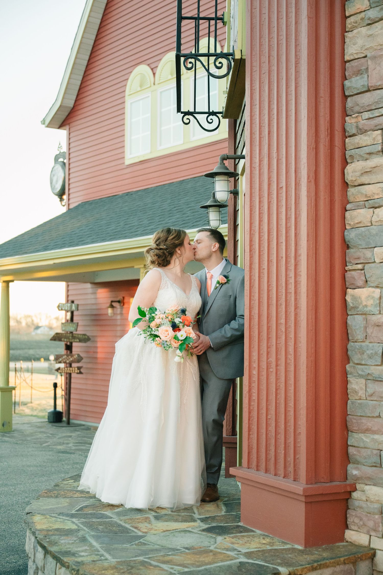 Bride and groom share a kiss outside a rustic red barn venue on their wedding day.