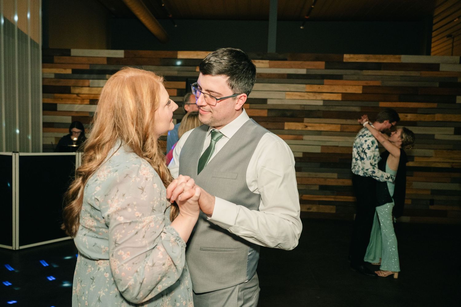 Couple shares a dance at a wedding reception in a modern venue with wood panel accent wall.