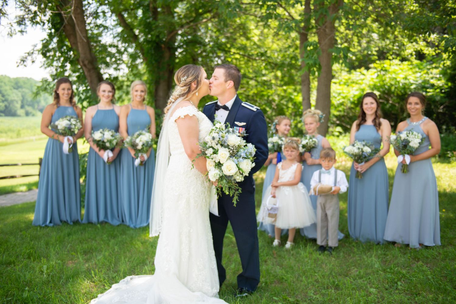 Wedding party in blue and white attire poses under trees during outdoor summer celebration. Zimmerman MN Weddings