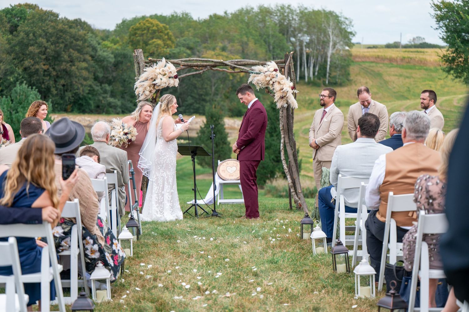 Panoramic view of an outdoor wedding ceremony with white chairs and guests on a hillside.