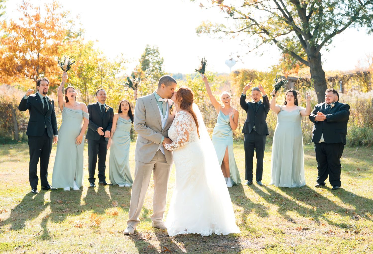 Central MN Wedding Photos | Bride and groom share a kiss surrounded by bridesmaids in mint dresses and groomsmen in black suits outdoors.