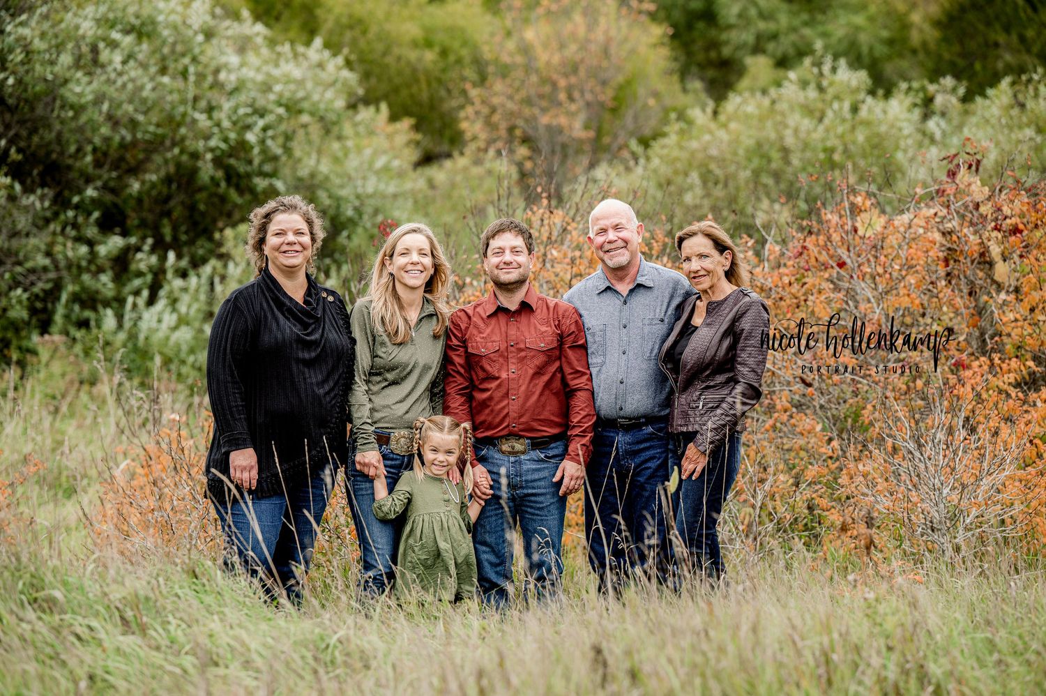 Extended family group poses together outdoors among fall foliage and tall grass.