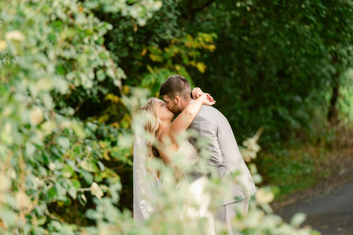 Central MN Wedding Photos | Bride and groom share a kiss surrounded by lush green foliage on wedding day.