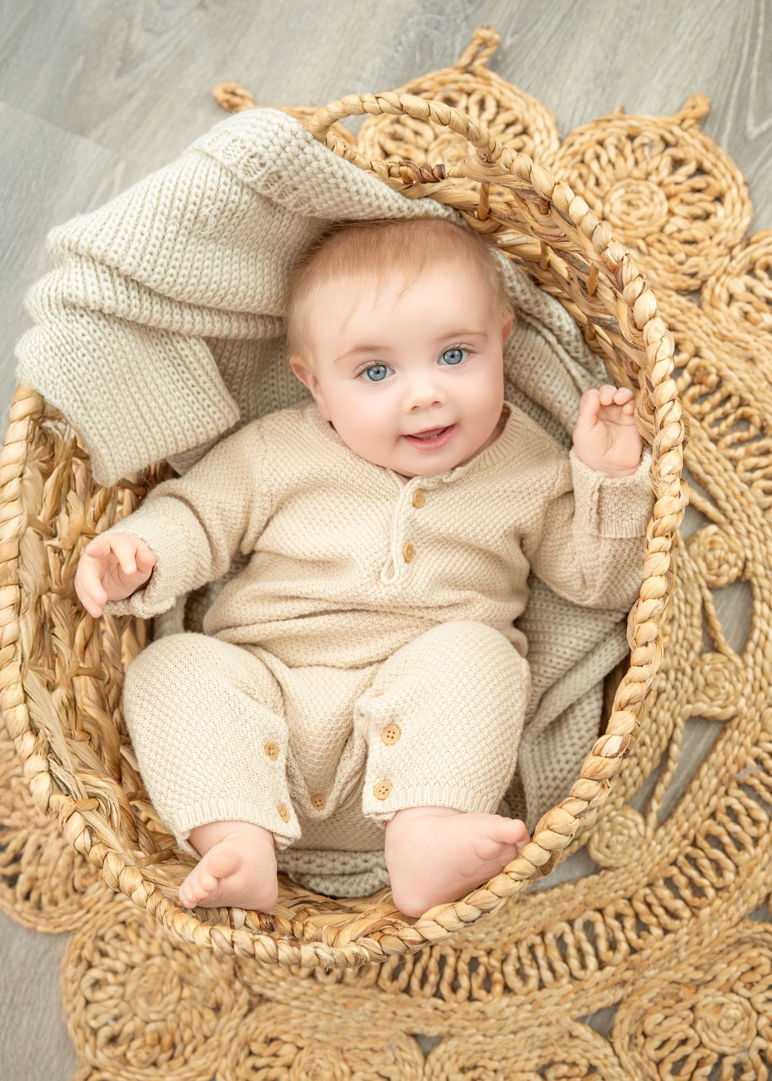 Central MN Milestone Photography -  baby with blue eyes in beige knit outfit sitting in a woven basket with a soft blanket.