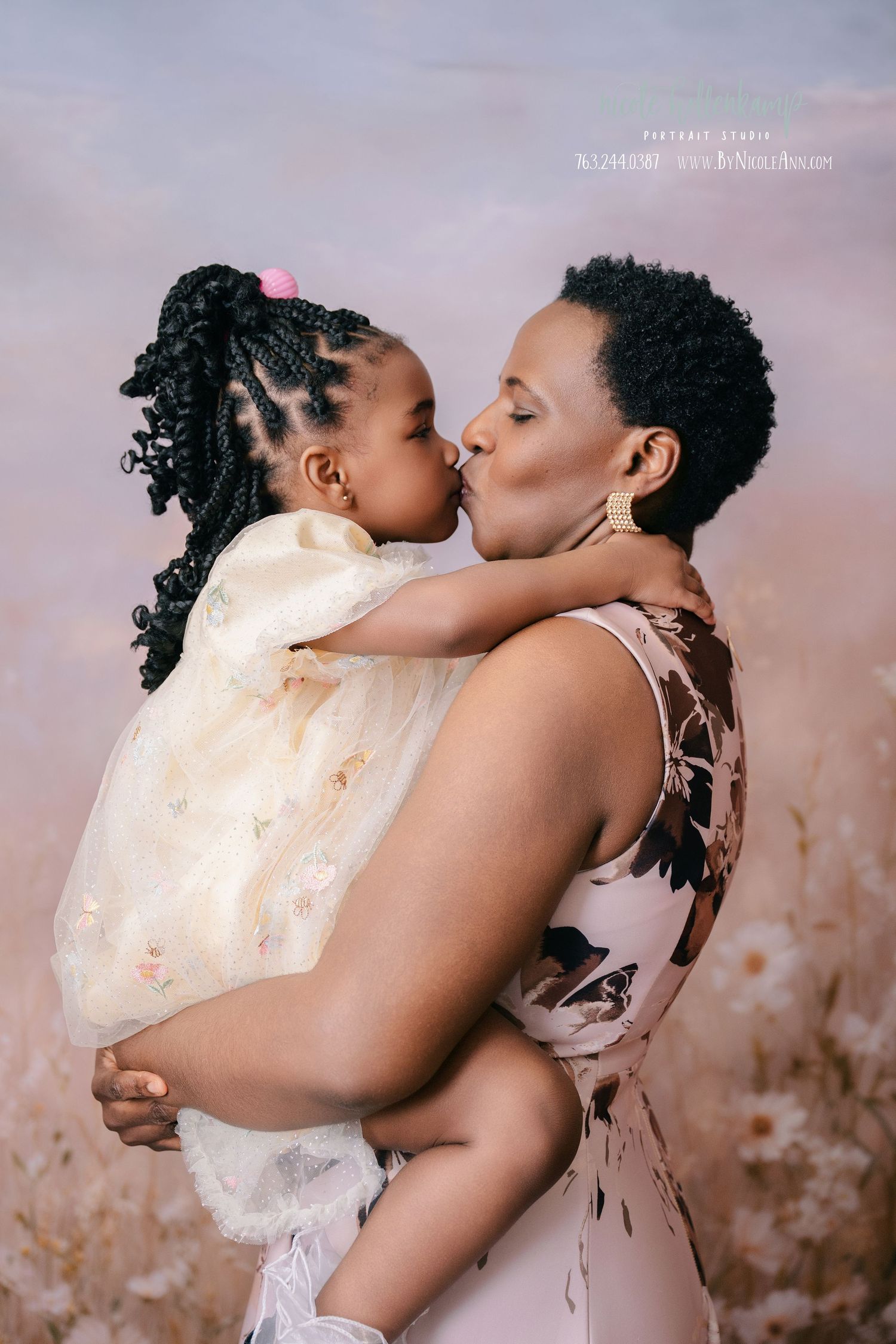 A mother holds and kisses her young daughter in a dreamy floral field portrait session. mother day photoshoot