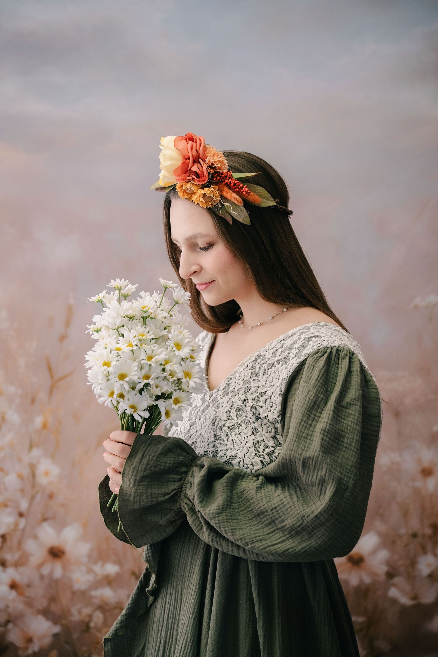 Young woman in green lace dress holding white daisies, wearing floral crown, standing in blooming field. mother day photoshoot