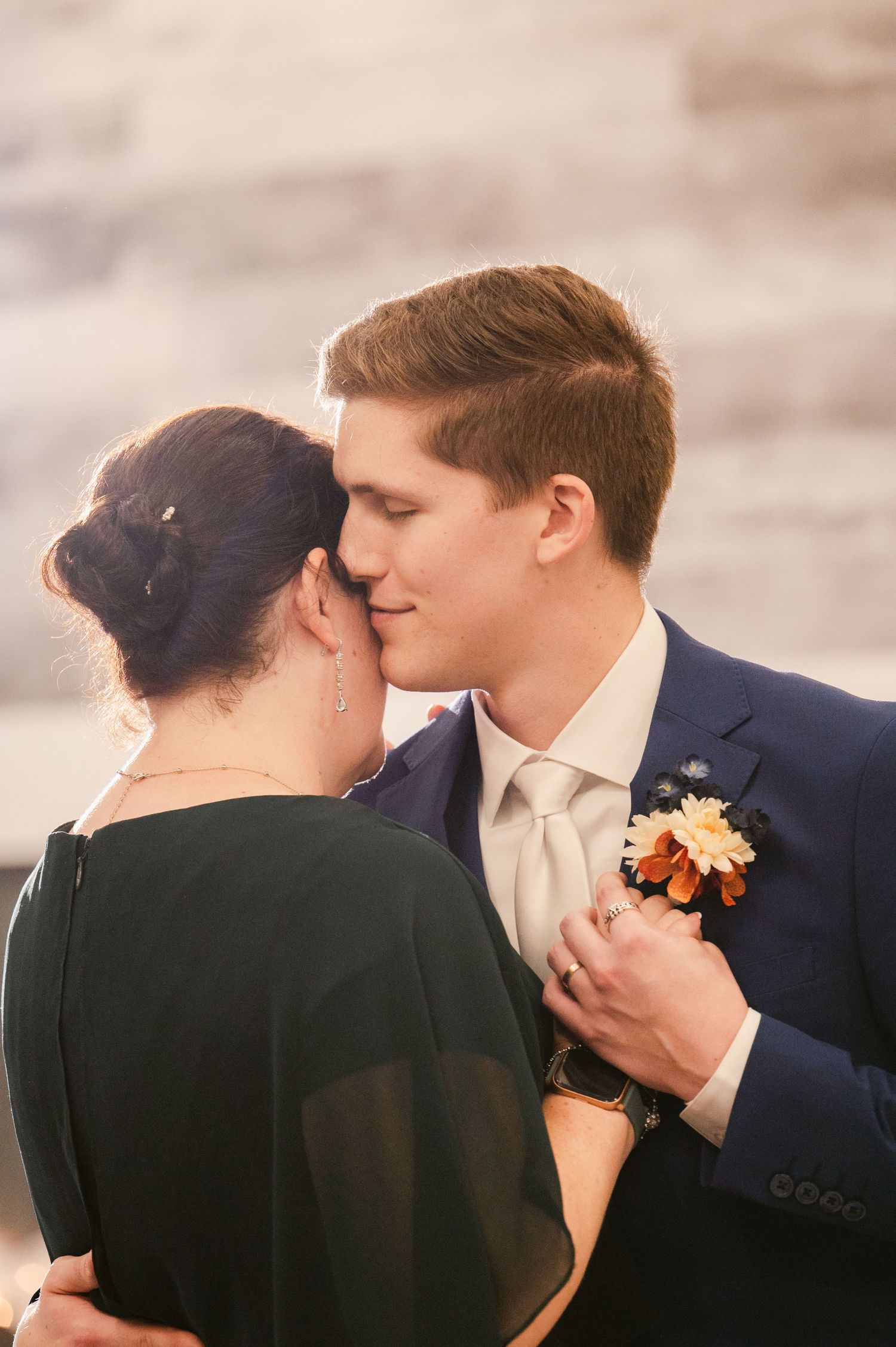 A romantic couple share an intimate dance moment at their wedding, with the groom wearing a navy suit and peach boutonniere.