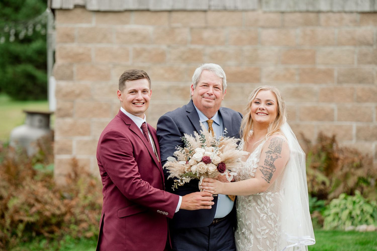 Wedding party poses together outside stone building with floral bouquets.