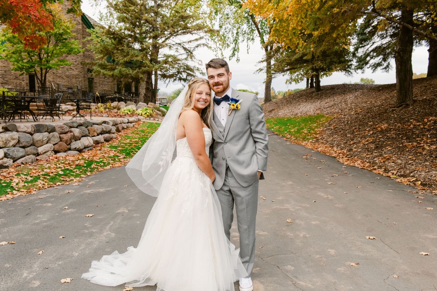 Central MN Wedding Photos | Smiling bride and groom posing outdoors in fall foliage, bride wearing veil and groom in gray suit.