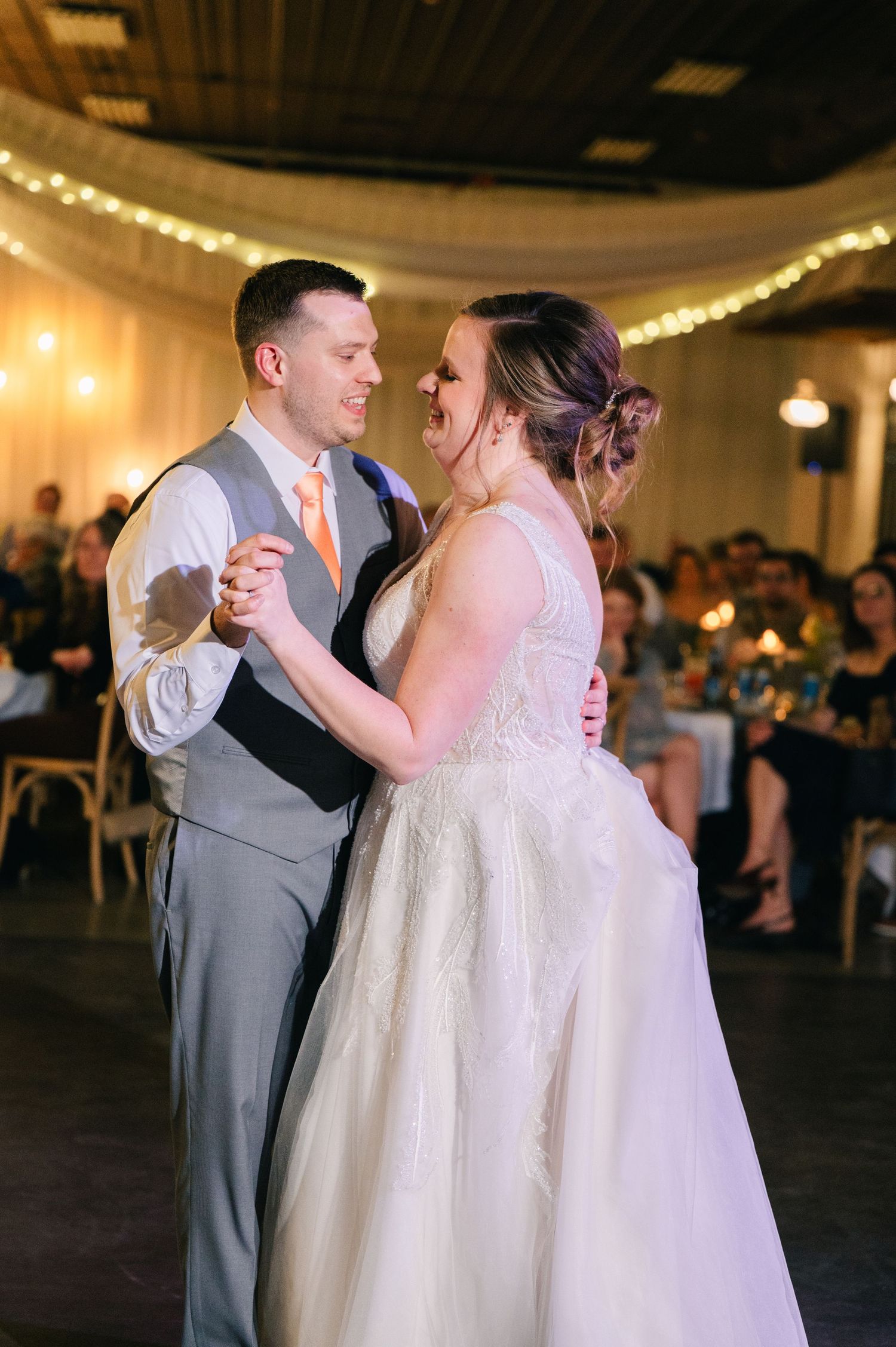 Bride and groom sharing their first dance in a warmly lit wedding reception venue.