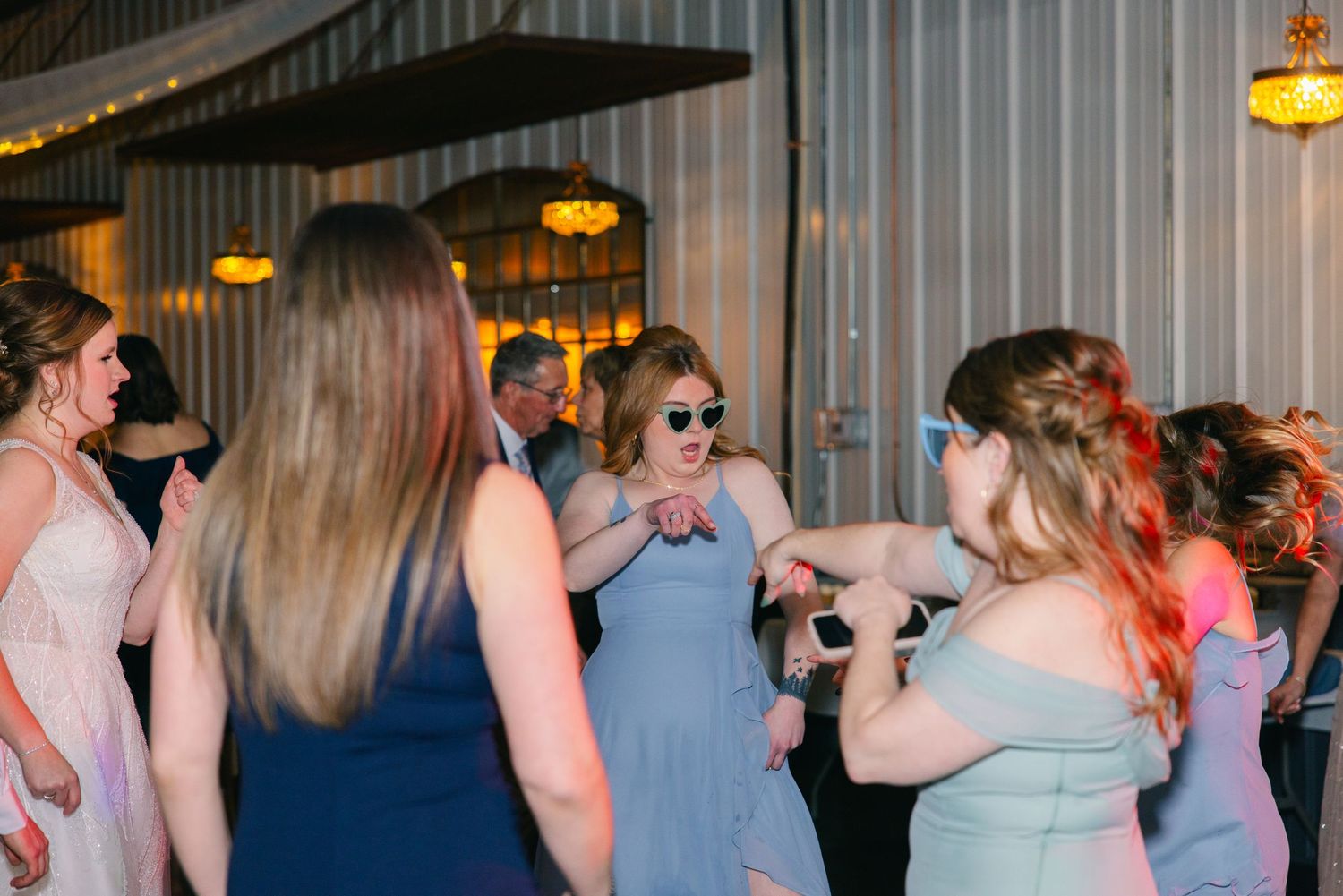 Bridesmaids in blue and pink gowns dance energetically at lively wedding reception celebration.