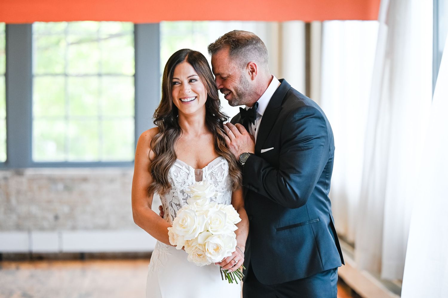 Couple sharing intimate moment during wedding celebration in bright indoor venue.