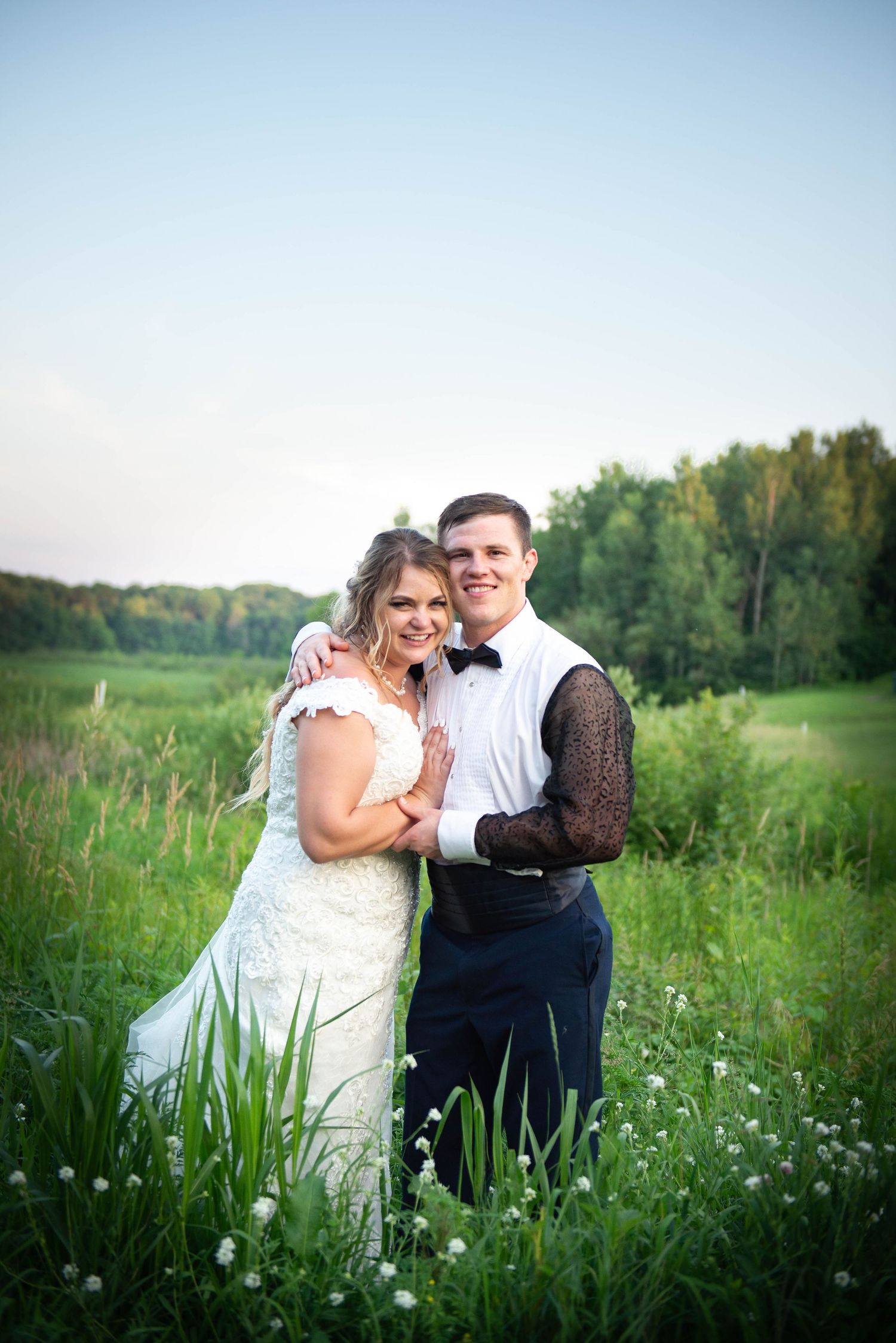 Wedding couple poses together in sunlit meadow with wildflowers. Zimmerman MN Weddings