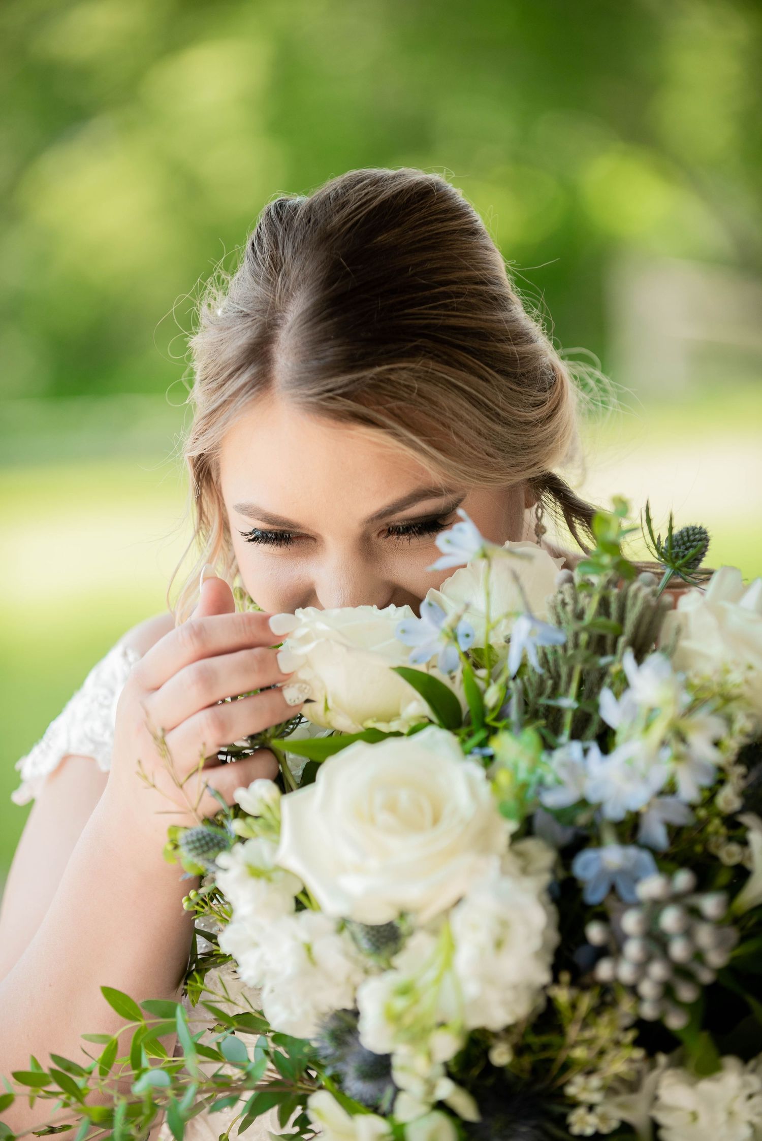 Elegant white and blue floral wedding bouquet held against soft green background. Zimmerman MN Weddings