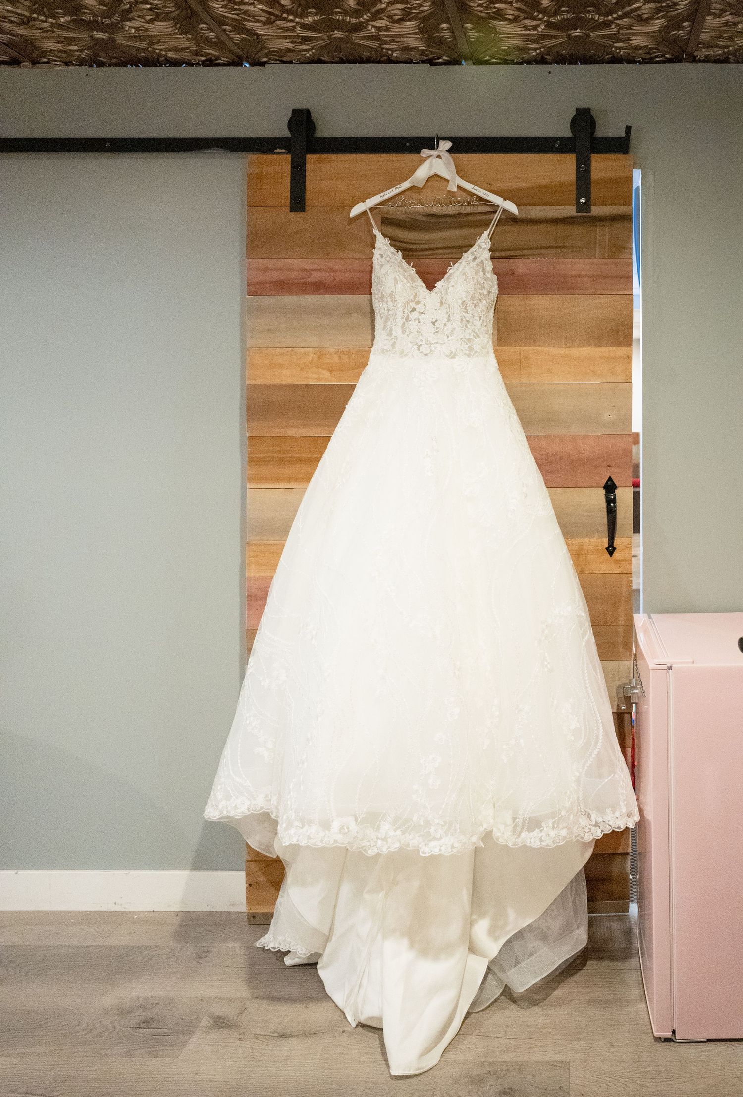 Stunning white lace ball gown wedding dress hanging on a rustic barn door in a bridal suite.