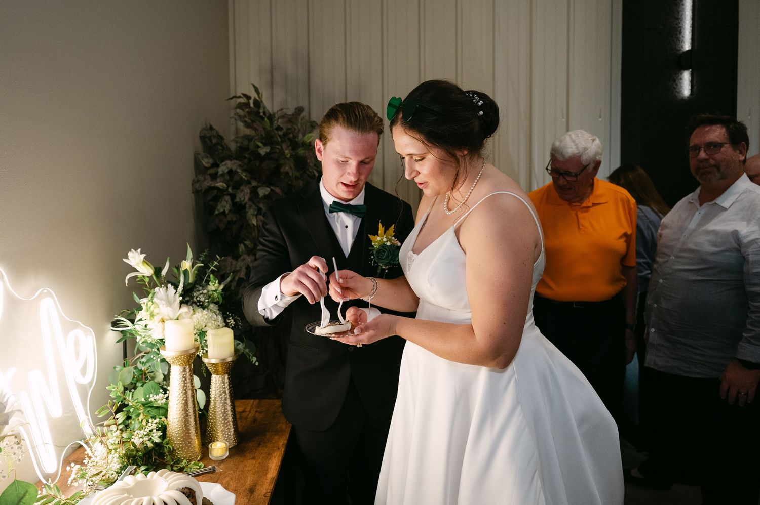 Wedding guests gather around a dimly lit reception area with white floral decorations and candles.