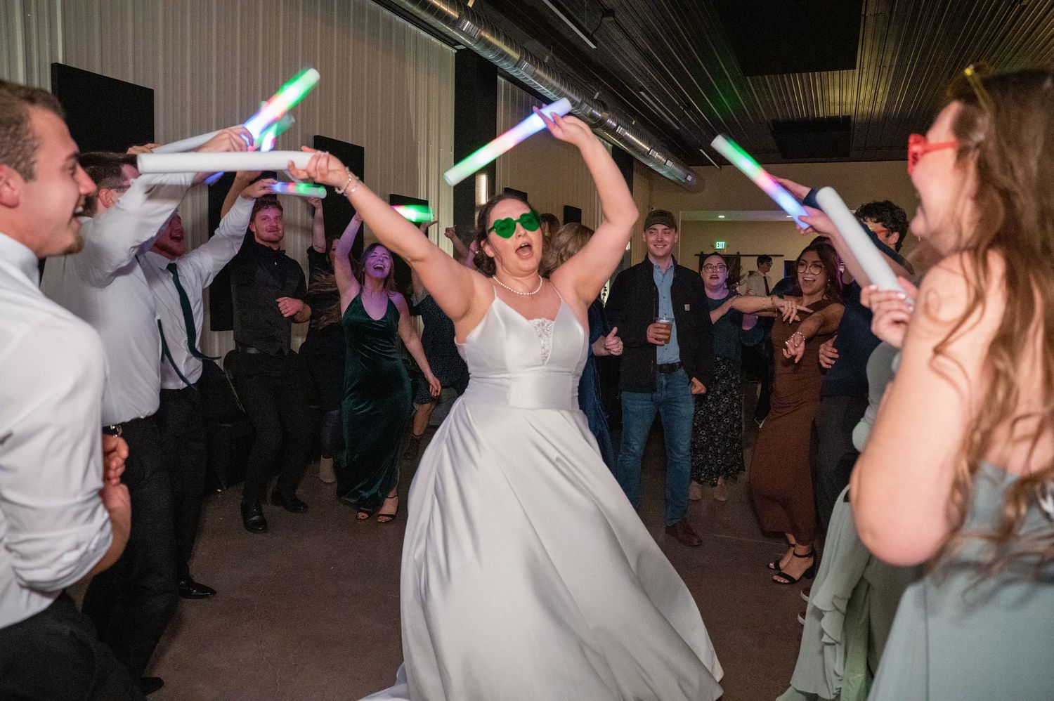 Wedding guests dancing with glowing neon light sticks raised in celebration on the dance floor.