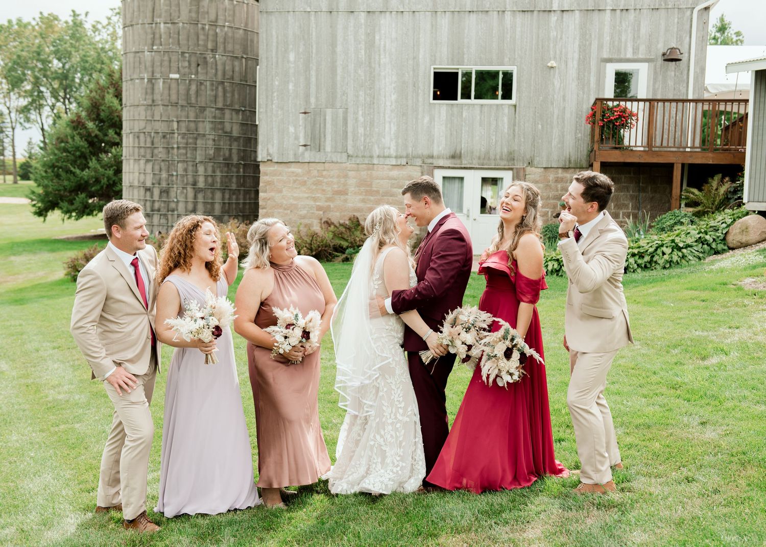 Wedding party wearing pink and burgundy attire walking together on a grassy lawn in elegant formation.