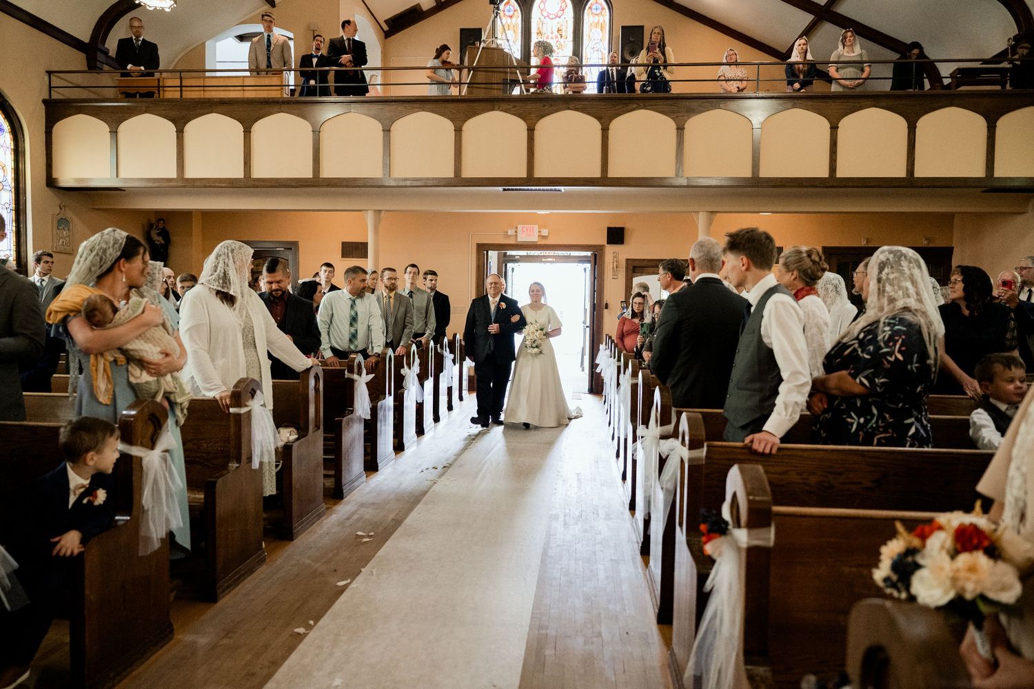 Wedding ceremony in a traditional church with elegant wooden pews and decorative arches lining the aisle.