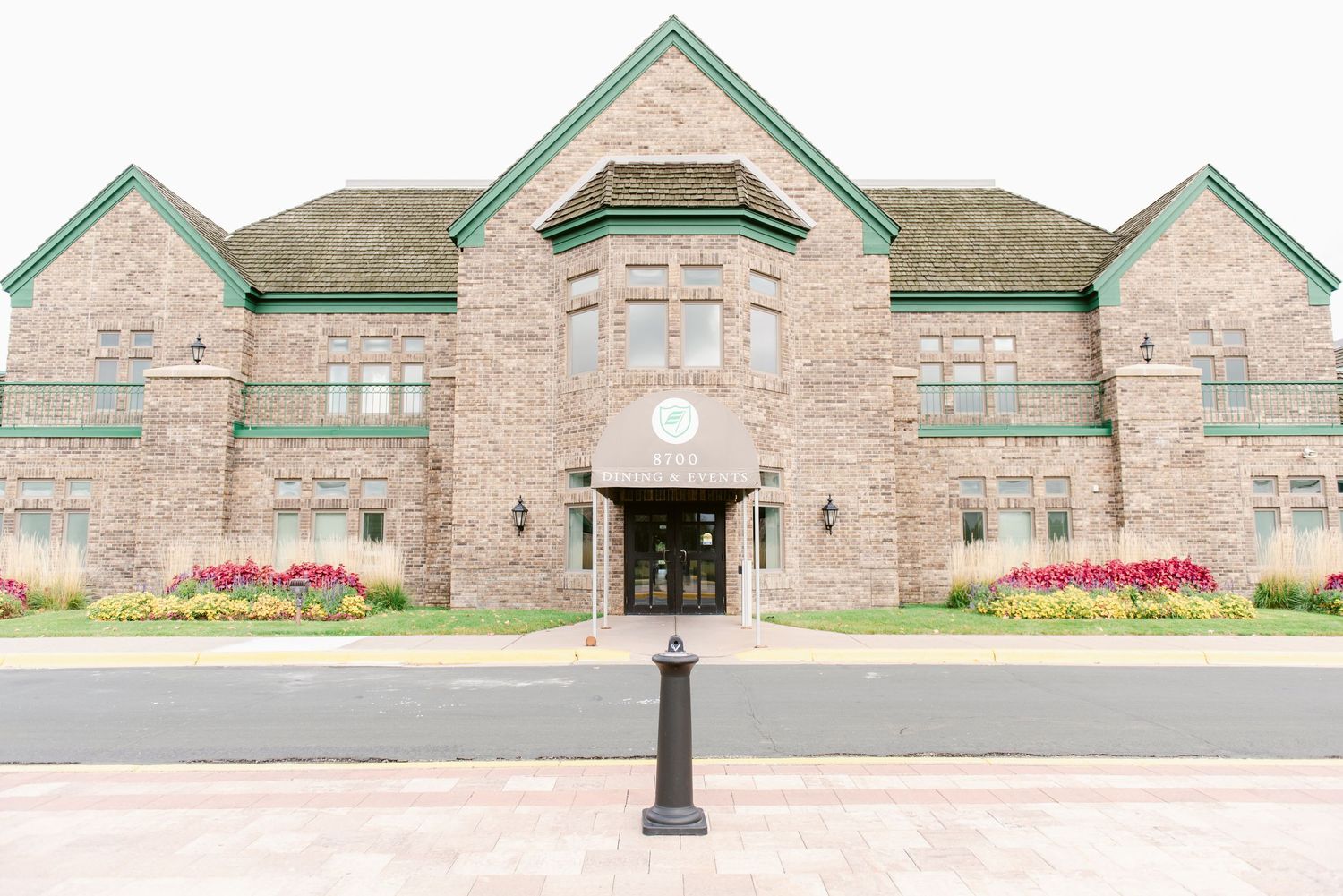 A panoramic view of a historic brick church building with red flowers and landscaping along the front entrance.