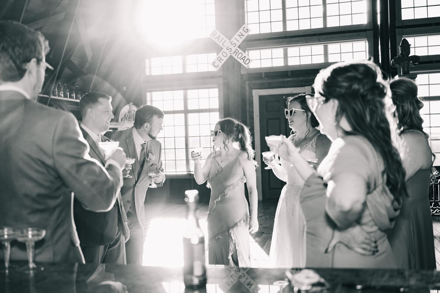 Black and white photo of wedding guests celebrating at rustic bar venue.