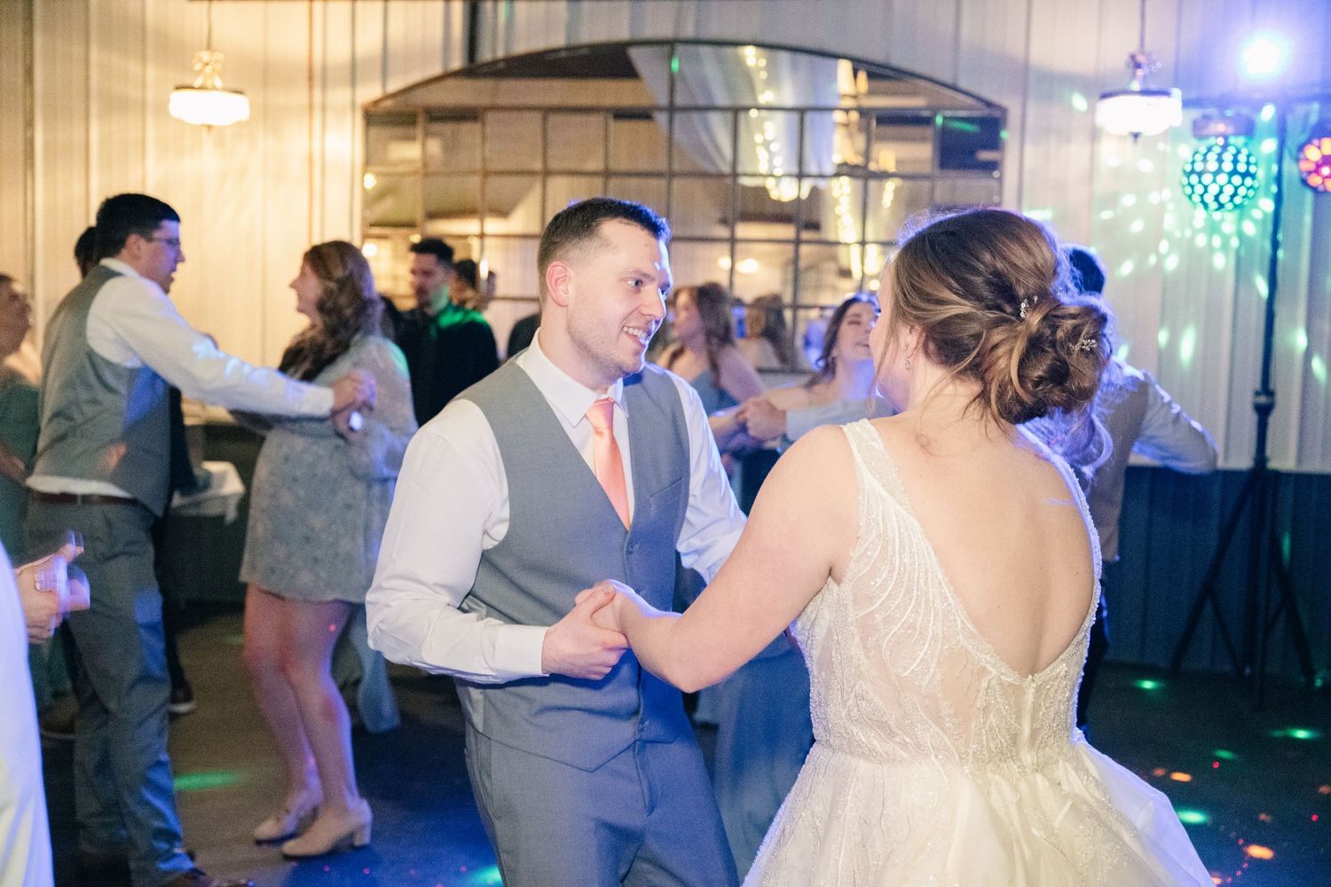 Bride and groom dance together under colorful lights at lively wedding reception celebration.