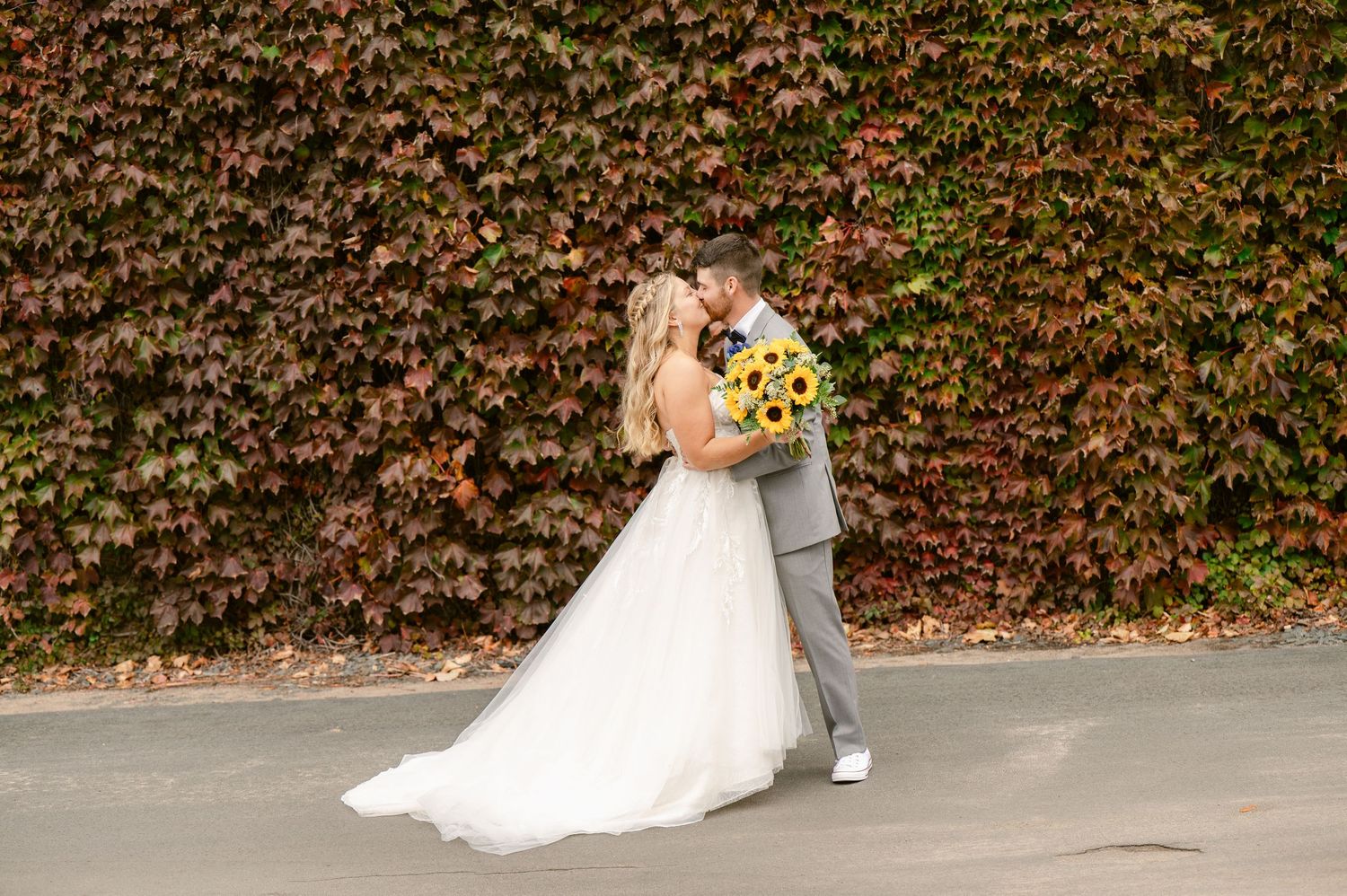 Central MN Wedding Photos | Bride and groom share a tender kiss in front of a red and green ivy-covered wall.