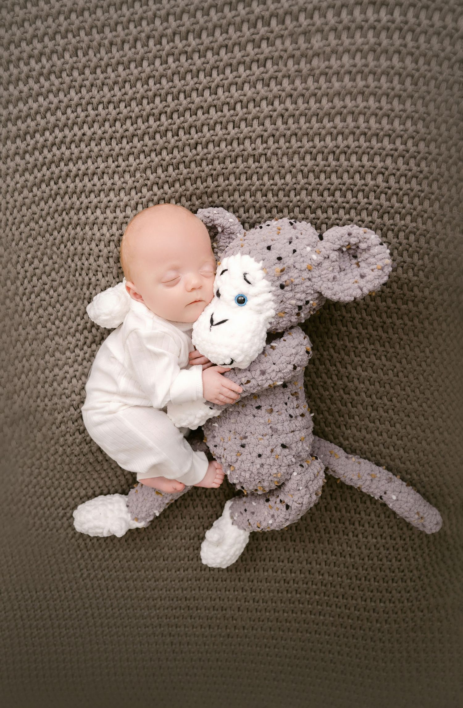 St Cloud newborn Photos of Sleeping newborn baby in white outfit cuddling a gray crocheted monkey stuffed animal on a knit blanket.