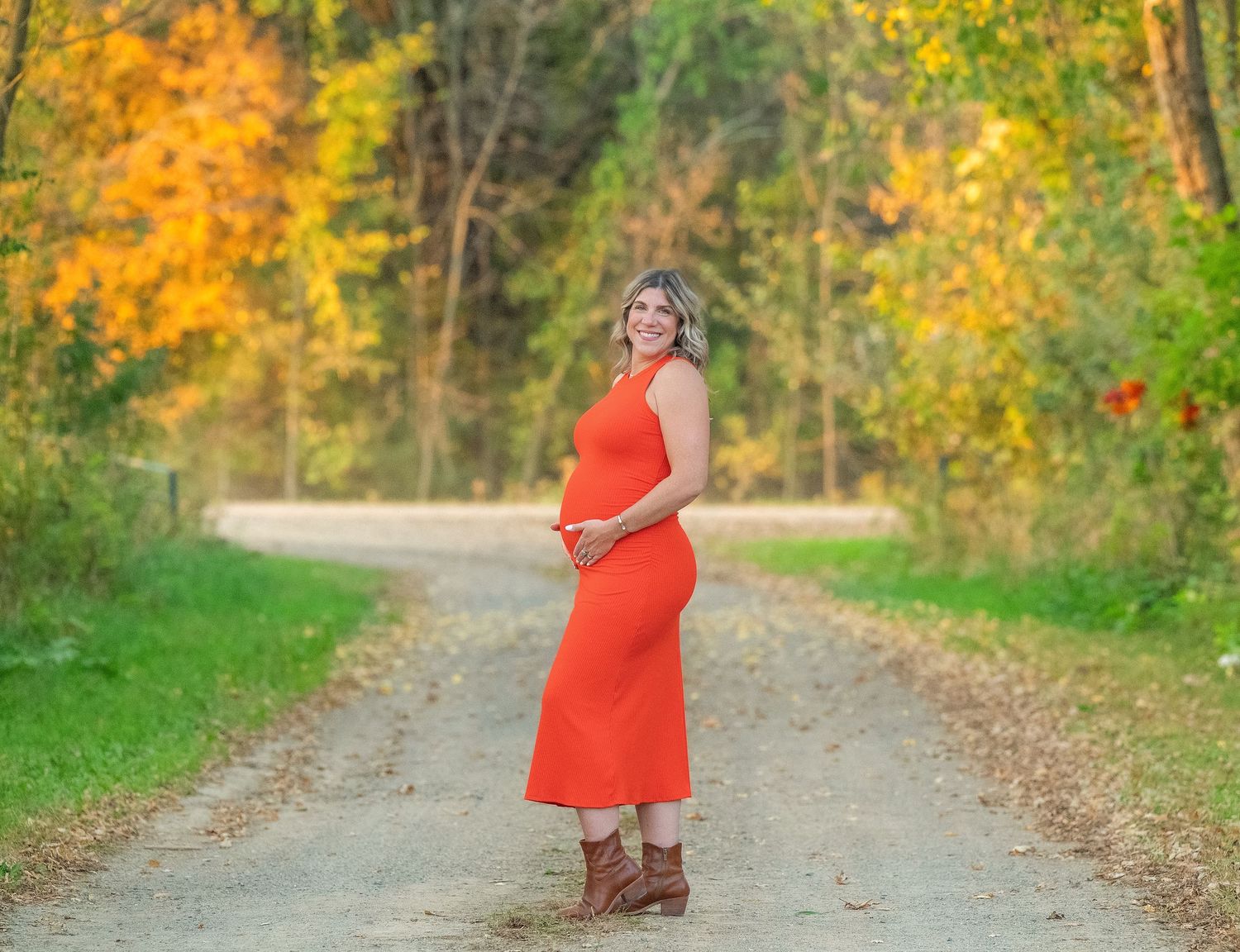 Scenic autumn path through colorful fall foliage with a person in a bright red dress walking.