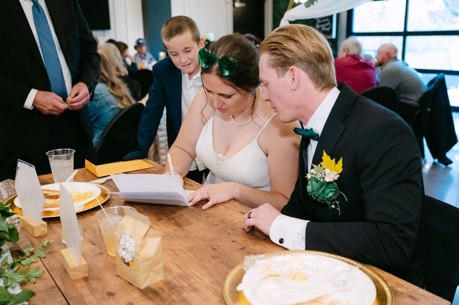 Wedding guests enjoy conversation and refreshments at rustic wooden tables during a reception.