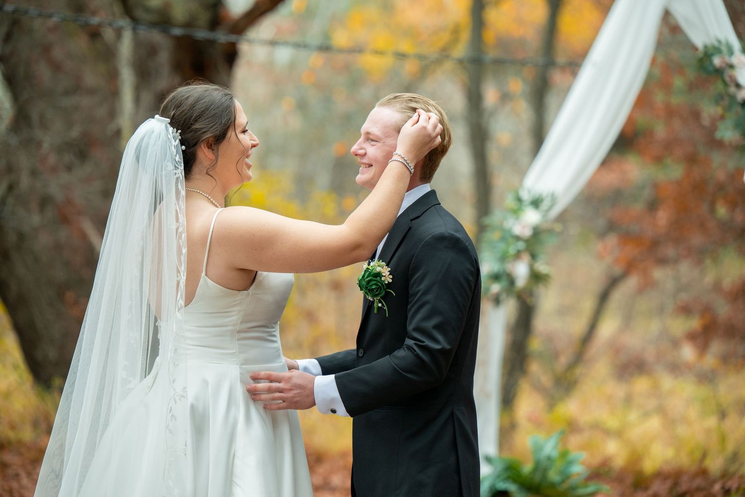 Newlyweds embrace and laugh together in a wooded setting with vibrant orange autumn leaves in the background.