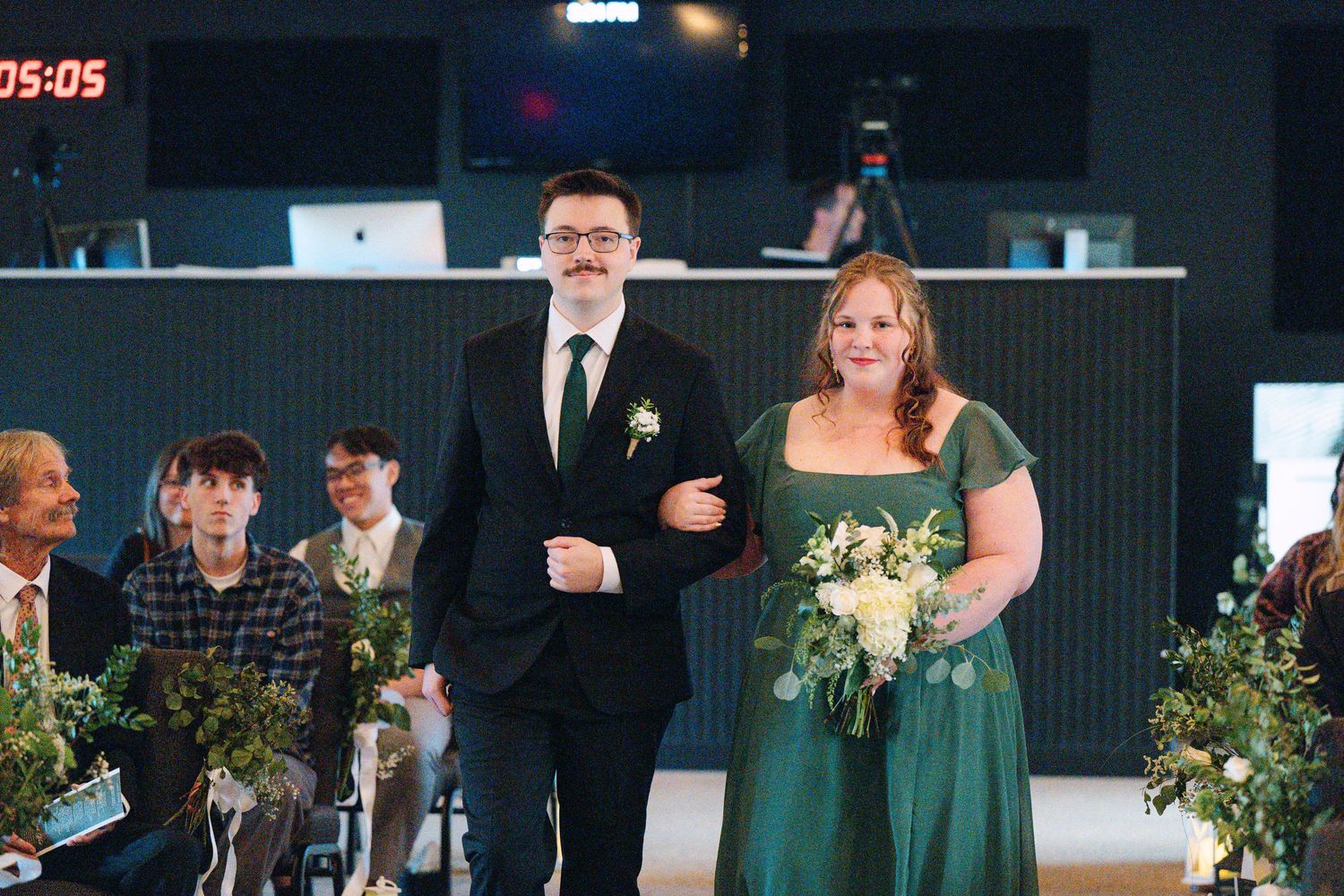 Wedding guests in formal attire gathered at an indoor venue with elegant lighting and decor.