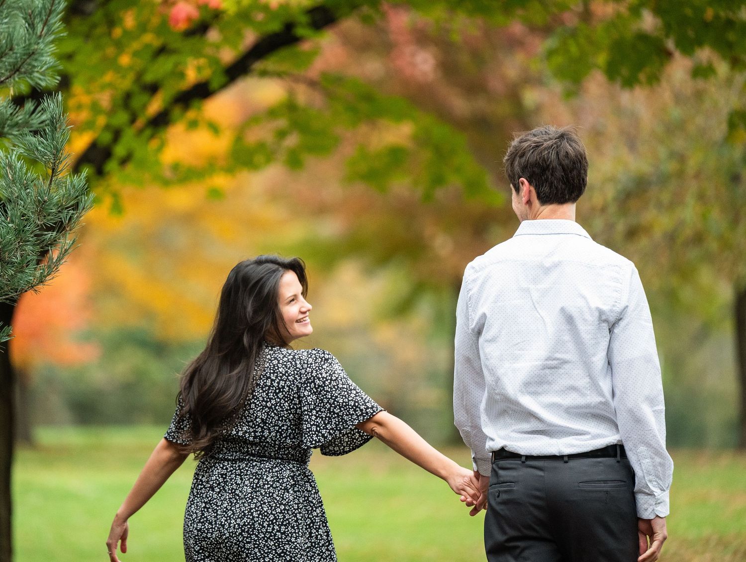 A couple holding hands and walking together in a park with autumn foliage in the background at Lake Como. Engagement Sessions Minnesota.