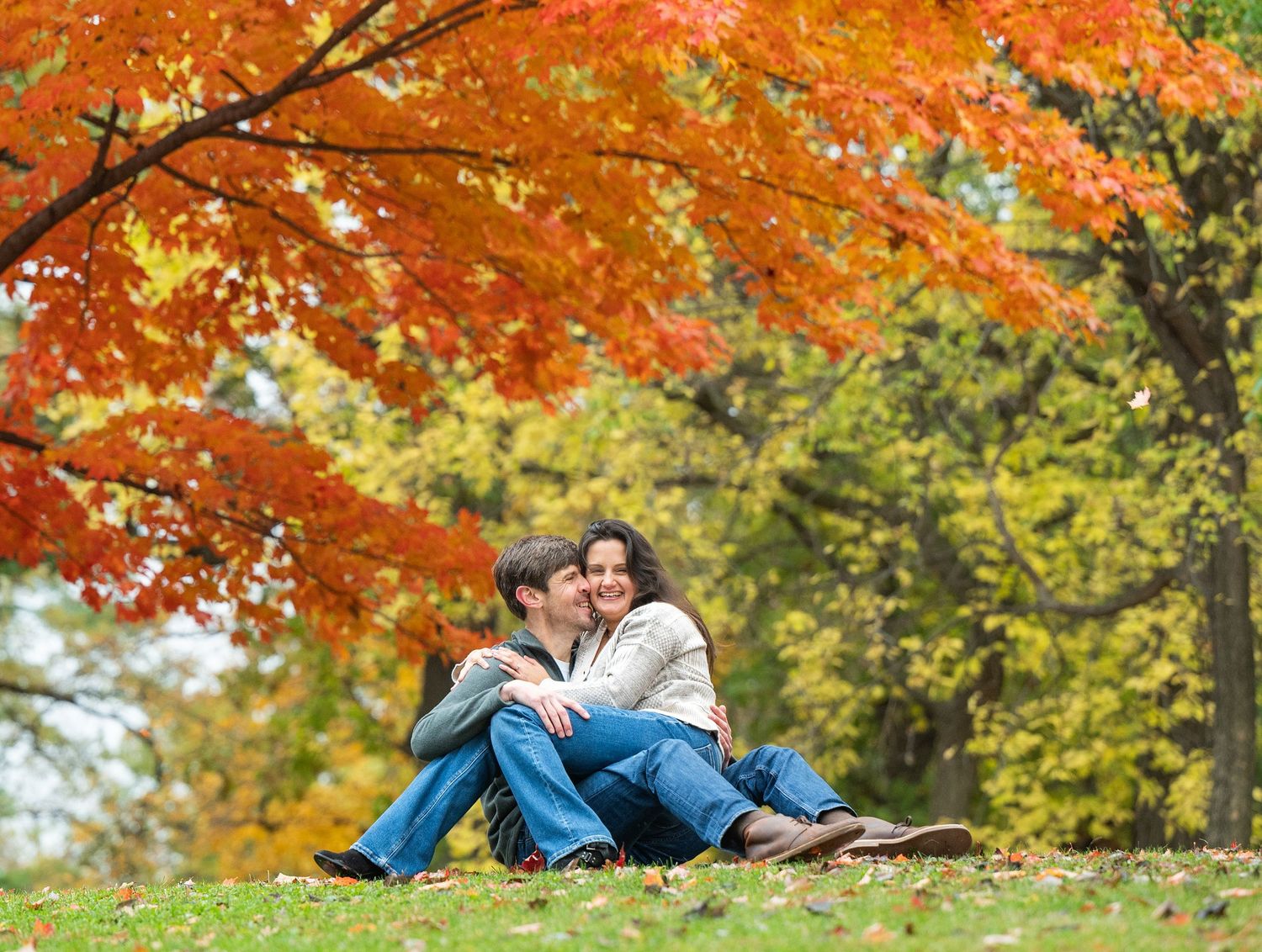 Two people relax under vibrant red and orange fall maple trees at Lake Como. Engagement Sessions Minnesota