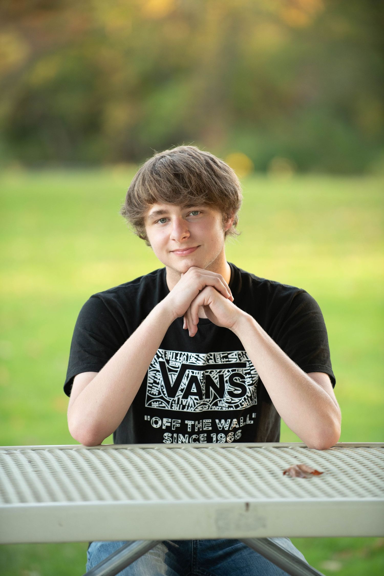 Casual portrait at a picnic table wearing a black Vans t-shirt against a green background.