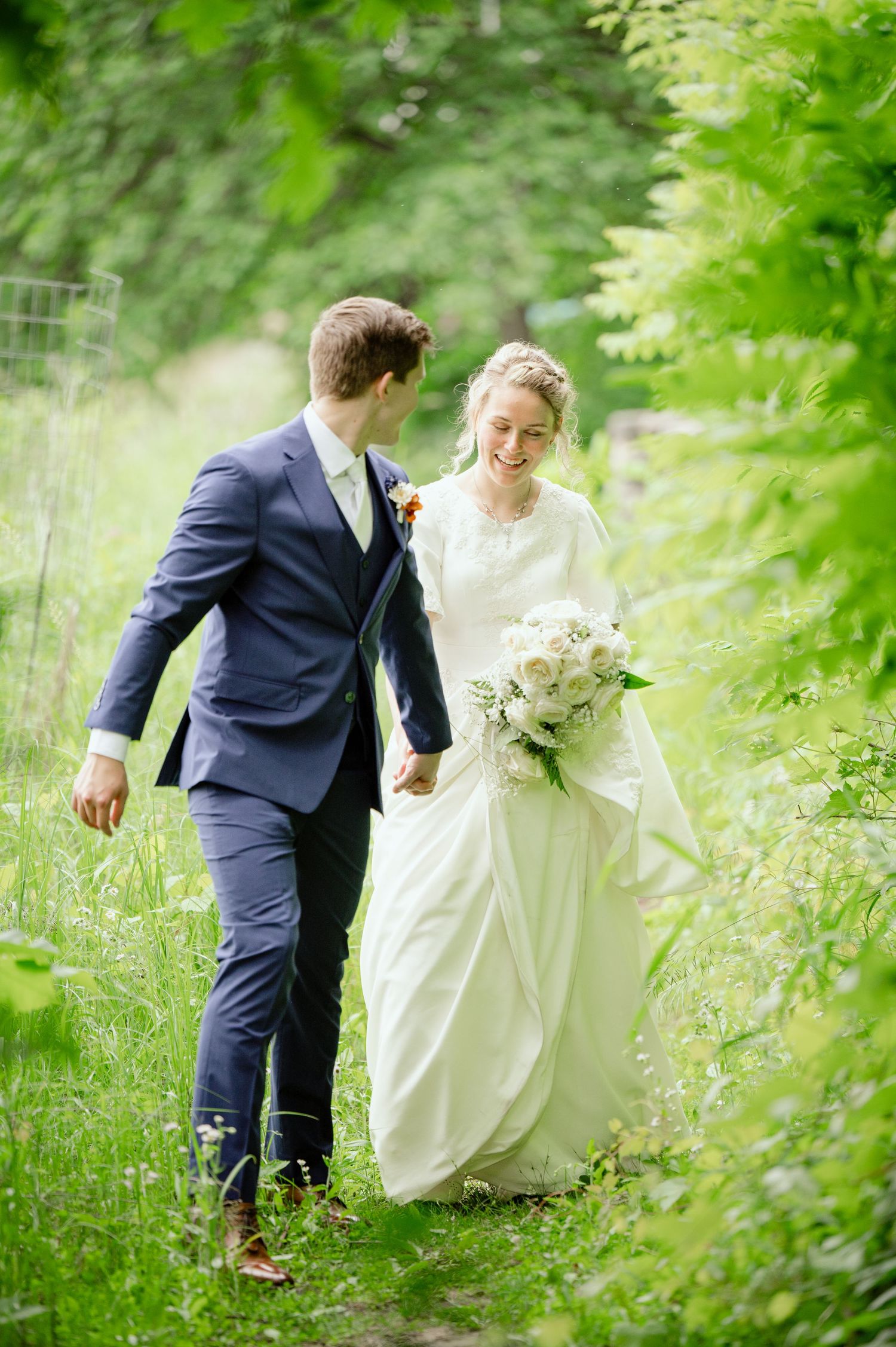 A couple walks hand in hand through a verdant garden path on their wedding day.