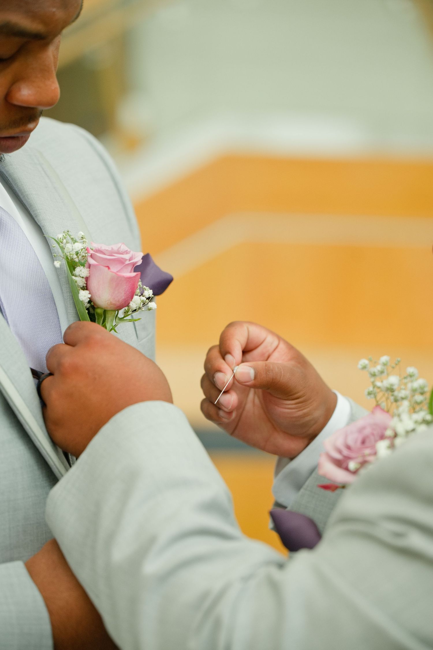 Groom in gray suit having pink rose boutonniere pinned to lapel at wedding ceremony.