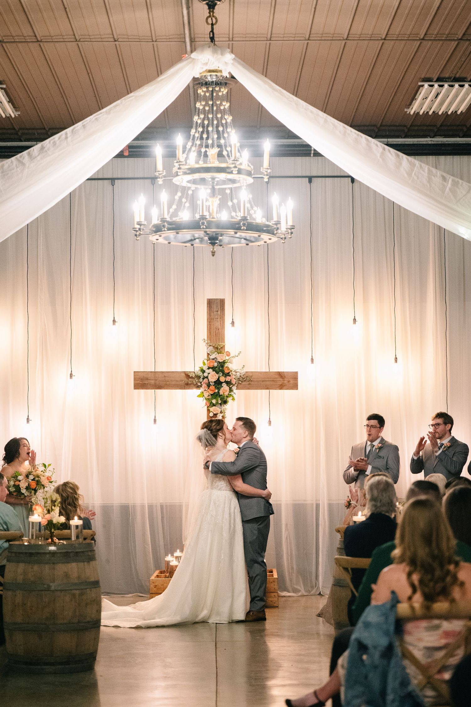 crooked willow weddings A couple shares their first dance beneath a chandelier and wooden cross at an elegant barn wedding reception.