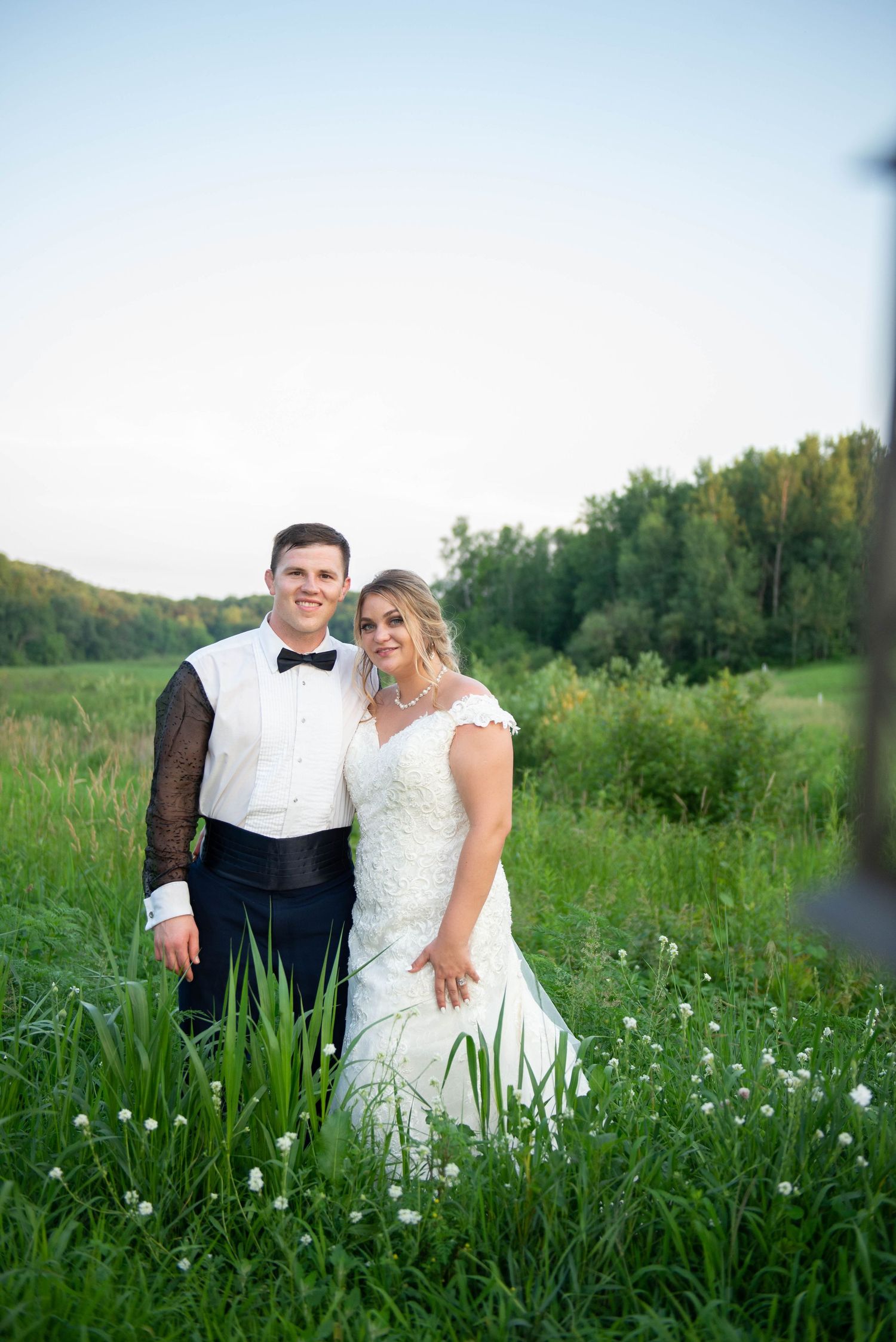 Newlyweds pose together in meadow with wildflowers during golden hour. Zimmerman MN Weddings