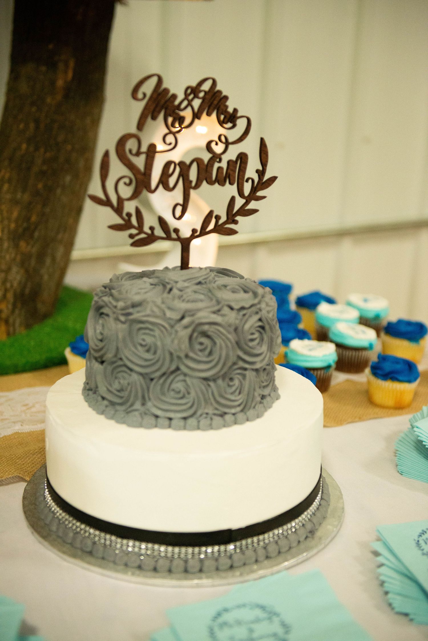 Two tiered wedding cake with white and grey rosette design topped with a decorative name topper. Zimmerman MN Weddings