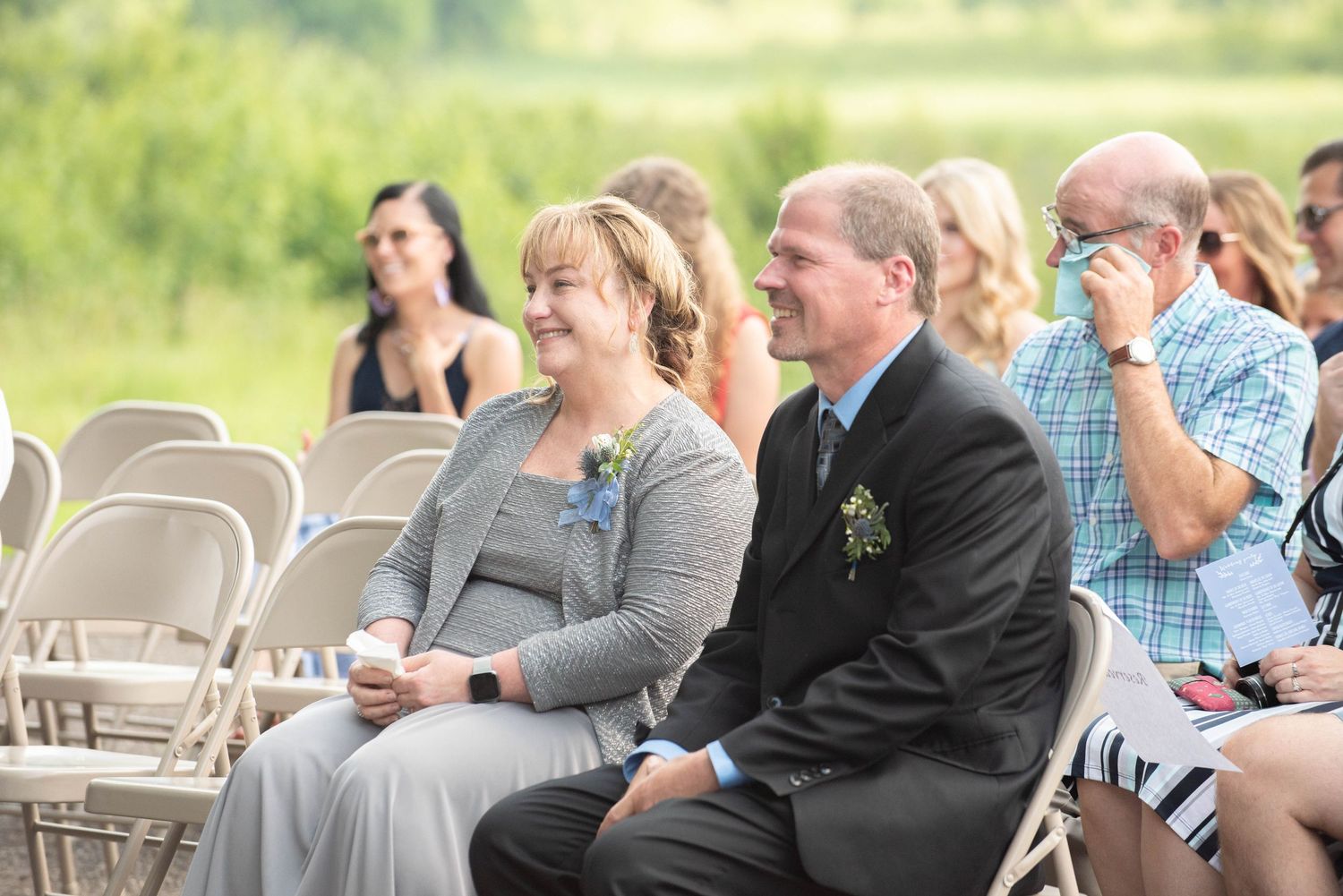 Rows of white chairs filled with guests at an outdoor gathering with trees in the background. Zimmerman MN Weddings